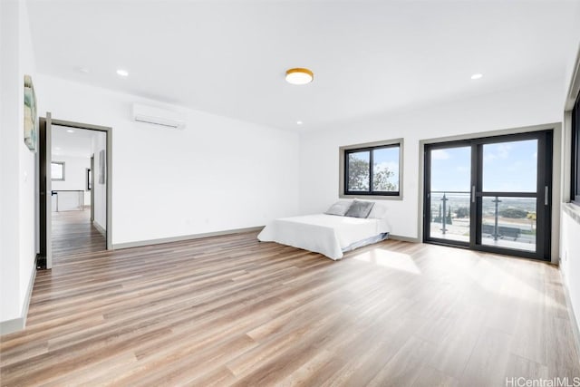 unfurnished bedroom featuring access to outside, a wall mounted AC, and light hardwood / wood-style flooring