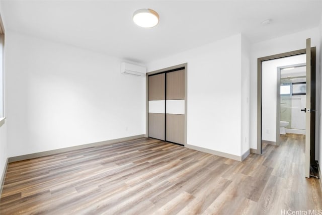 unfurnished bedroom with a closet, light hardwood / wood-style floors, and an AC wall unit