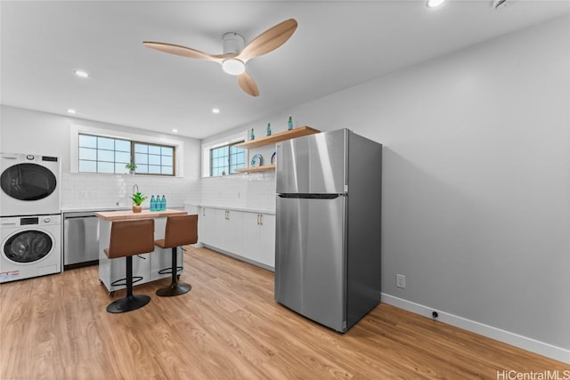 kitchen with light hardwood / wood-style flooring, stacked washing maching and dryer, stainless steel appliances, white cabinets, and a kitchen bar