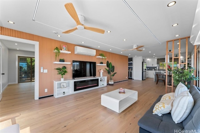 living room with ceiling fan, a wall mounted air conditioner, and light hardwood / wood-style flooring