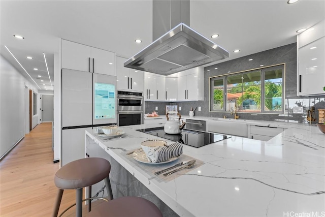 kitchen with light stone counters, island exhaust hood, white cabinets, and appliances with stainless steel finishes