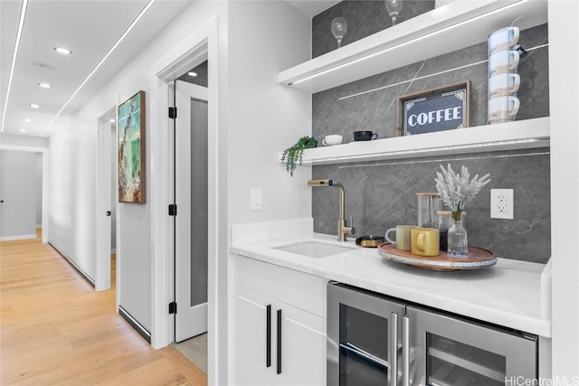 bar with sink, white cabinets, wine cooler, decorative backsplash, and light hardwood / wood-style floors