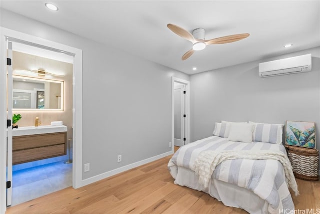 bedroom with a wall mounted air conditioner, ensuite bathroom, ceiling fan, and light wood-type flooring