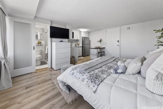 bedroom featuring a textured ceiling, stainless steel fridge, light wood-type flooring, and ensuite bath