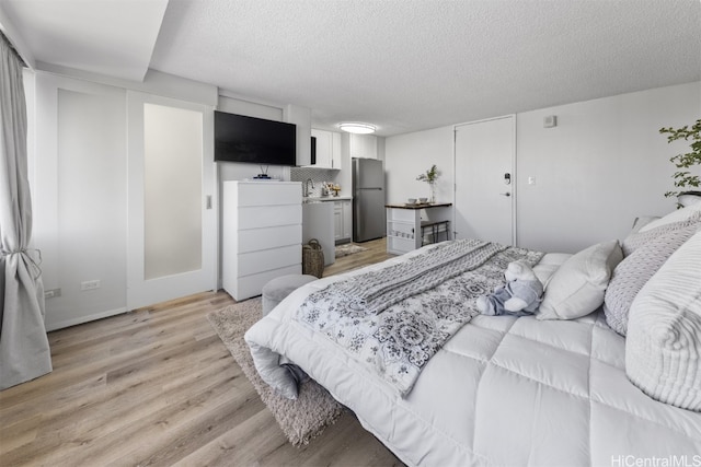 bedroom with light wood-type flooring, a textured ceiling, and stainless steel refrigerator