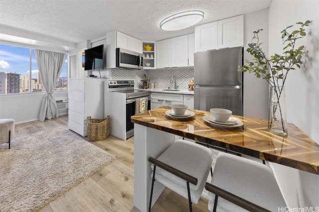 kitchen featuring white cabinetry, stainless steel appliances, wooden counters, and a breakfast bar area