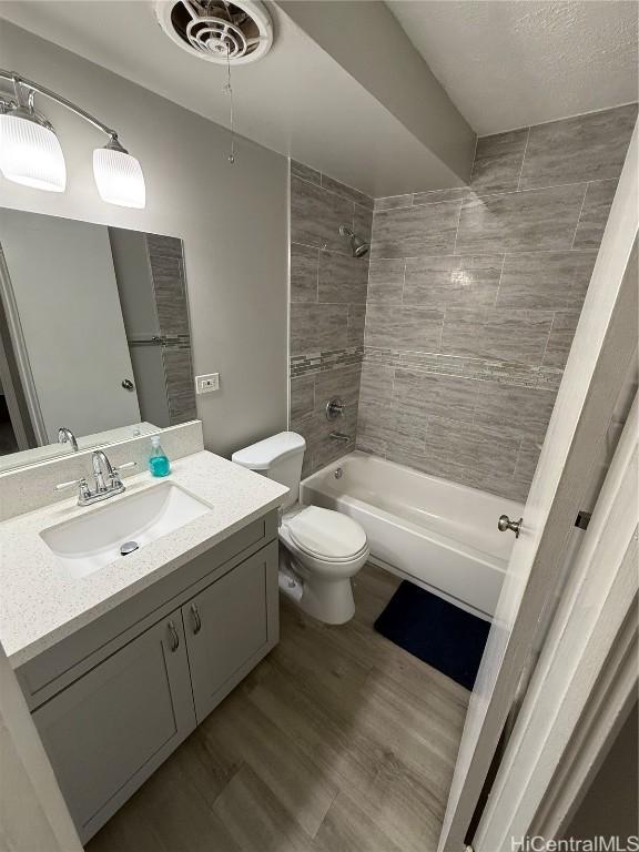 full bathroom with vanity, tiled shower / bath, hardwood / wood-style floors, and toilet