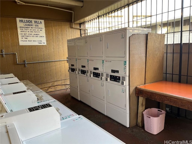 washroom featuring stacked washer and dryer, washing machine and dryer, and wood walls