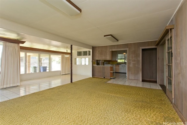 unfurnished living room featuring light tile patterned floors, wooden walls, and light colored carpet