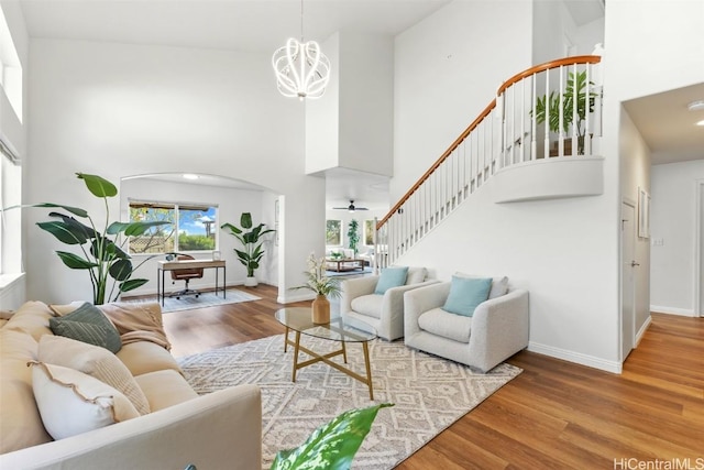 living room with wood-type flooring, a towering ceiling, and ceiling fan with notable chandelier