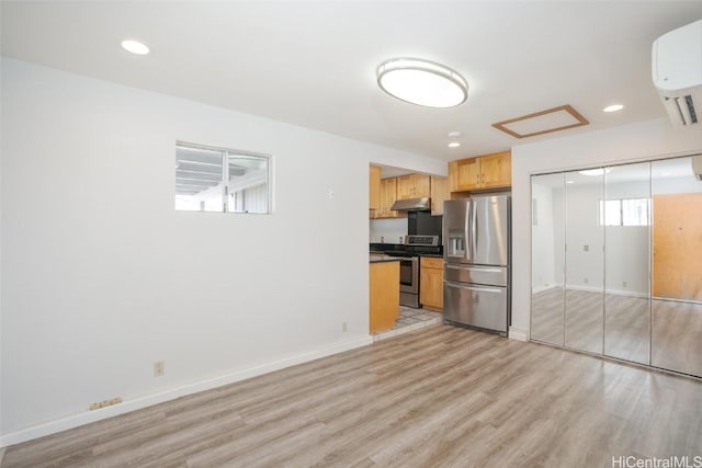 kitchen with stainless steel appliances, a wall mounted AC, light brown cabinets, and light hardwood / wood-style flooring