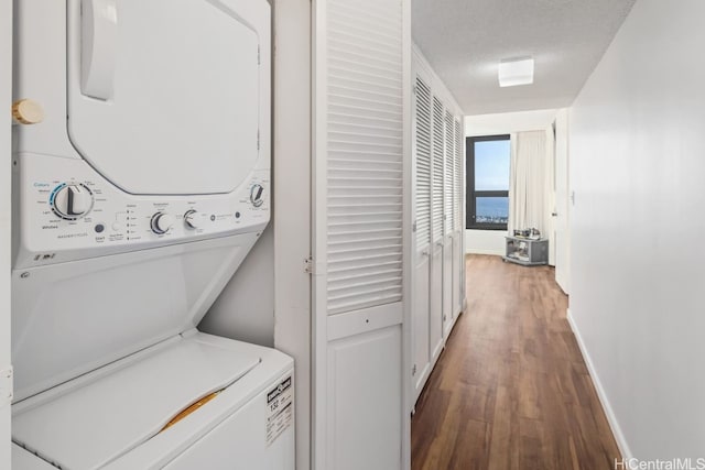 laundry room with dark wood-type flooring, stacked washing maching and dryer, and a textured ceiling