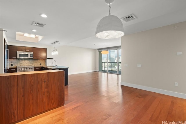 kitchen featuring pendant lighting, sink, kitchen peninsula, stainless steel appliances, and light hardwood / wood-style flooring