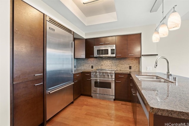 kitchen with sink, decorative backsplash, hanging light fixtures, high end appliances, and dark brown cabinets