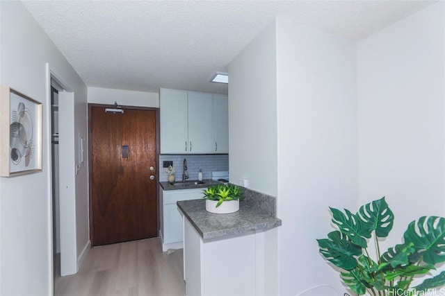 kitchen with light hardwood / wood-style flooring, a textured ceiling, decorative backsplash, sink, and white cabinetry