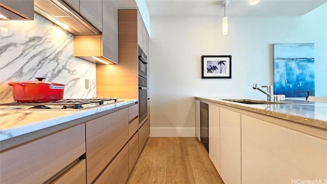 kitchen with pendant lighting, tasteful backsplash, stainless steel gas stovetop, sink, and light hardwood / wood-style flooring