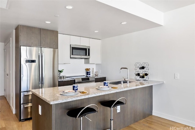 kitchen featuring a breakfast bar, white cabinetry, stainless steel appliances, light stone countertops, and light wood-type flooring