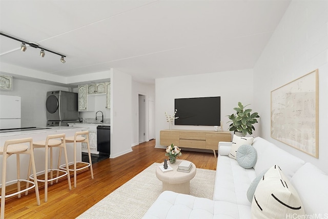 living room with wood-type flooring, rail lighting, sink, and stacked washer / drying machine