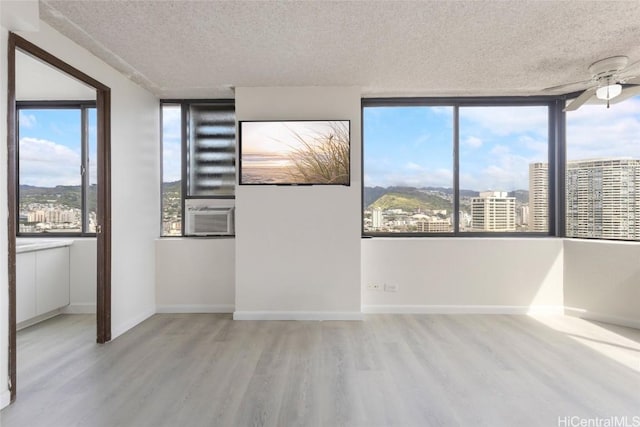 spare room featuring cooling unit, ceiling fan, a textured ceiling, and light wood-type flooring