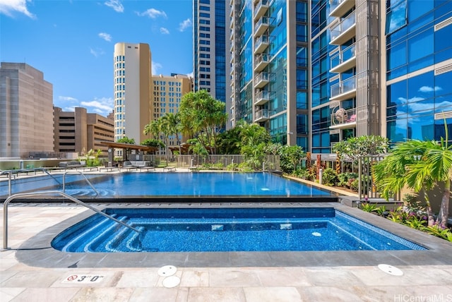 view of swimming pool with a hot tub, a view of city, and fence