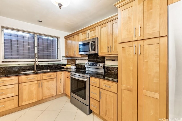 kitchen with appliances with stainless steel finishes, sink, dark stone countertops, and light brown cabinets