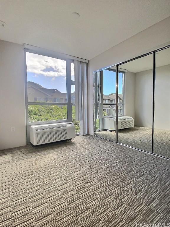 unfurnished bedroom featuring a closet, a wall mounted AC, carpet floors, and multiple windows