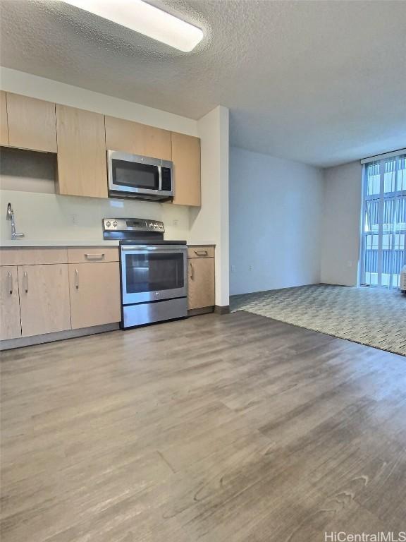 kitchen featuring light brown cabinetry, sink, a textured ceiling, appliances with stainless steel finishes, and light hardwood / wood-style floors