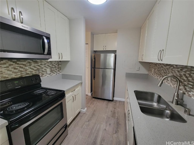 kitchen with tasteful backsplash, sink, white cabinets, stainless steel appliances, and light hardwood / wood-style flooring