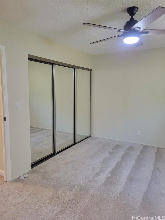 unfurnished bedroom featuring ceiling fan, light carpet, a textured ceiling, and a closet