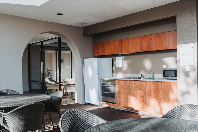 583 Kamoku St Unit 1907, Honolulu, HI 96826 - kitchen with oven, stainless steel microwave, freestanding refrigerator, brown cabinetry, and arched walkways