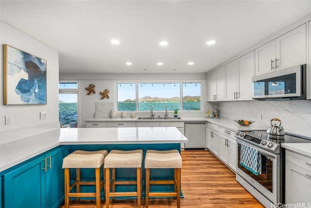 kitchen with sink, a water view, a kitchen breakfast bar, stainless steel appliances, and white cabinets