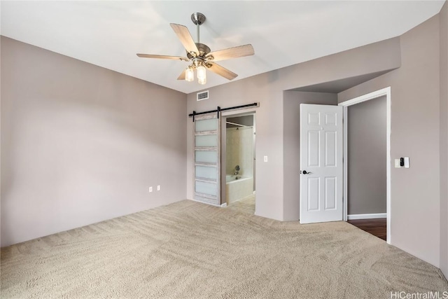 unfurnished bedroom featuring a barn door, carpet flooring, ceiling fan, and ensuite bath