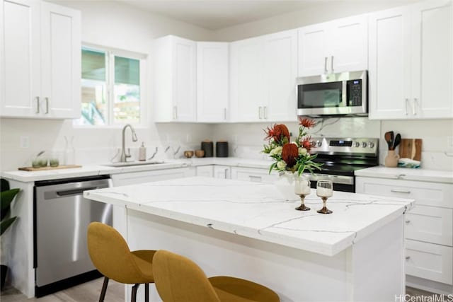 kitchen with sink, a center island, appliances with stainless steel finishes, a kitchen breakfast bar, and white cabinets