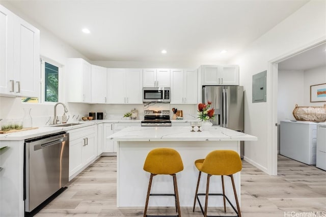 kitchen with sink, washer and clothes dryer, white cabinetry, stainless steel appliances, and a kitchen island