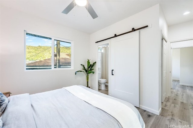 bedroom with ensuite bath, a barn door, ceiling fan, and light wood-type flooring