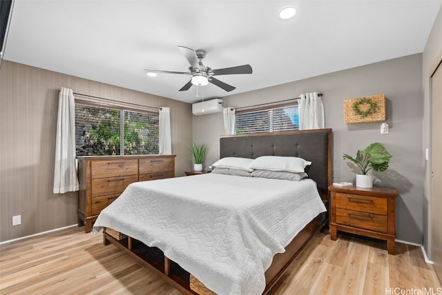 bedroom with ceiling fan, a wall unit AC, and light wood-type flooring