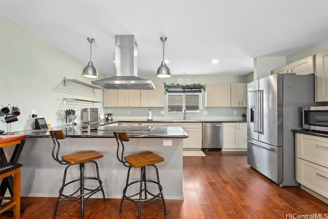 kitchen with sink, hanging light fixtures, stainless steel appliances, island exhaust hood, and a kitchen bar