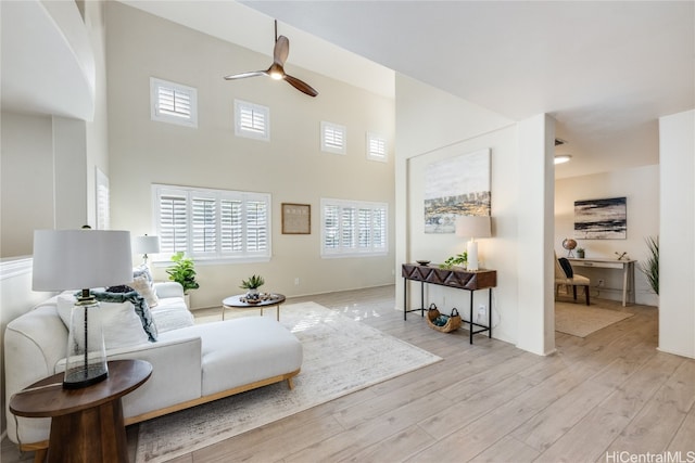 sitting room featuring ceiling fan, light hardwood / wood-style floors, and a towering ceiling