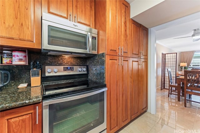 kitchen featuring ceiling fan, appliances with stainless steel finishes, light tile patterned flooring, decorative backsplash, and dark stone counters