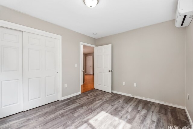 unfurnished bedroom featuring a closet, a wall mounted air conditioner, and light hardwood / wood-style flooring