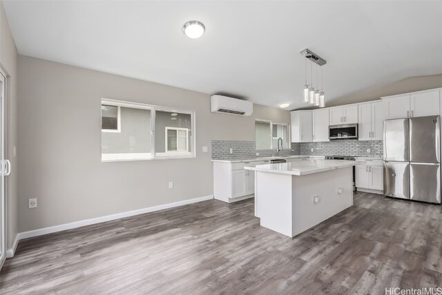 kitchen featuring hanging light fixtures, a wall unit AC, stainless steel appliances, white cabinets, and a kitchen island