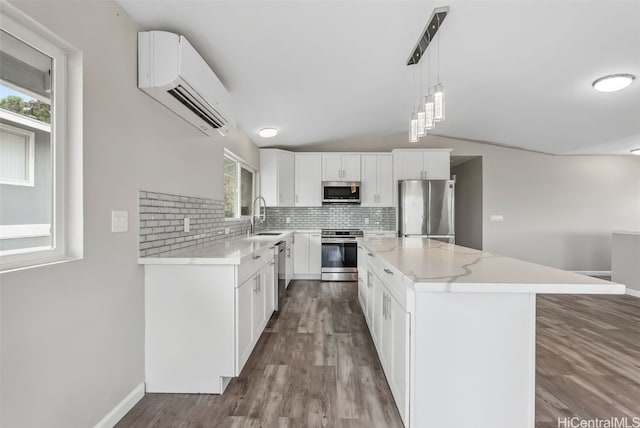 kitchen with appliances with stainless steel finishes, sink, a wall mounted AC, white cabinets, and a center island