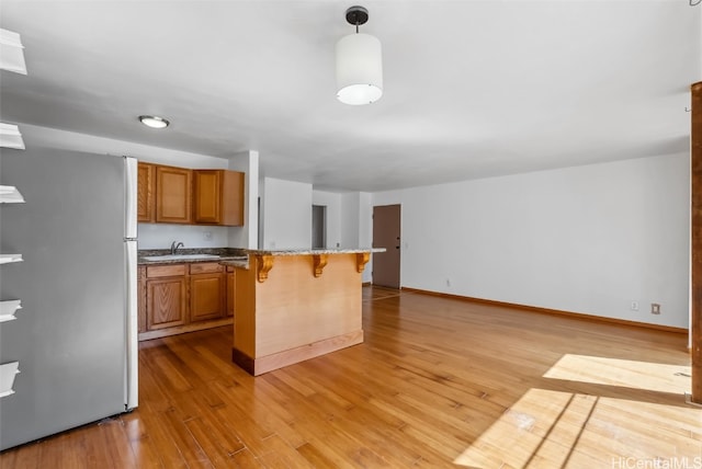 kitchen featuring brown cabinetry, a breakfast bar area, freestanding refrigerator, and light wood-style floors