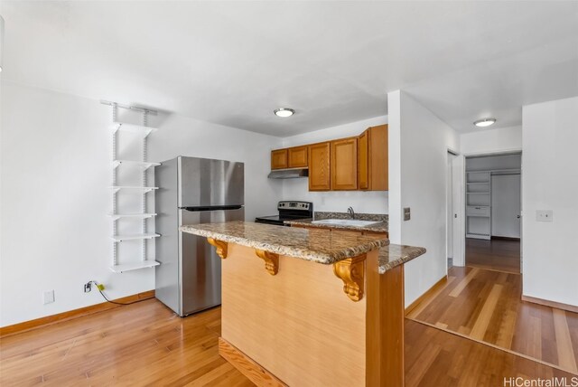 kitchen featuring a breakfast bar, sink, stone countertops, light hardwood / wood-style flooring, and appliances with stainless steel finishes