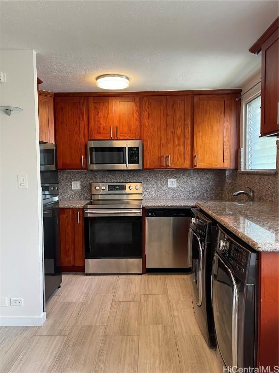 kitchen with backsplash, appliances with stainless steel finishes, washer / dryer, and stone counters