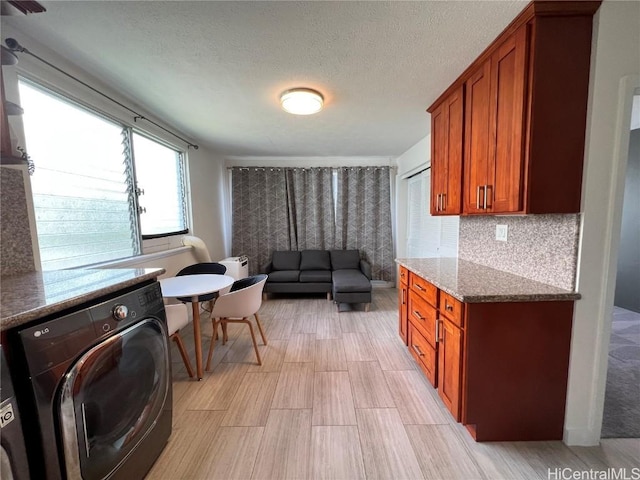 kitchen with backsplash, washer / dryer, a textured ceiling, and stone countertops