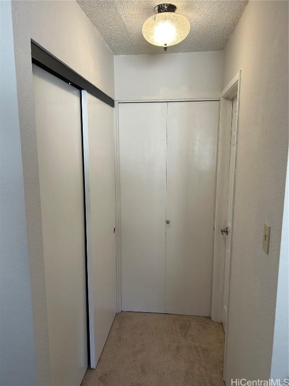 corridor with light colored carpet and a textured ceiling