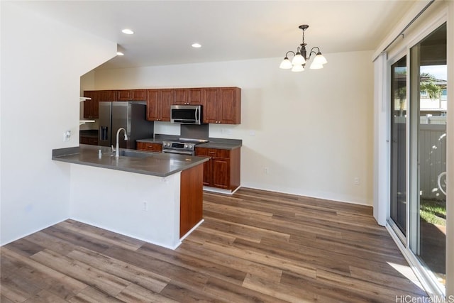 kitchen with appliances with stainless steel finishes, sink, dark hardwood / wood-style flooring, hanging light fixtures, and kitchen peninsula