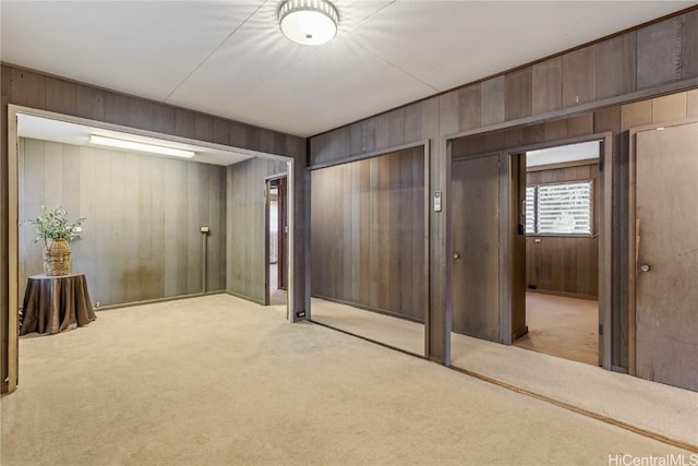 interior space with light carpet, two closets, and wood walls