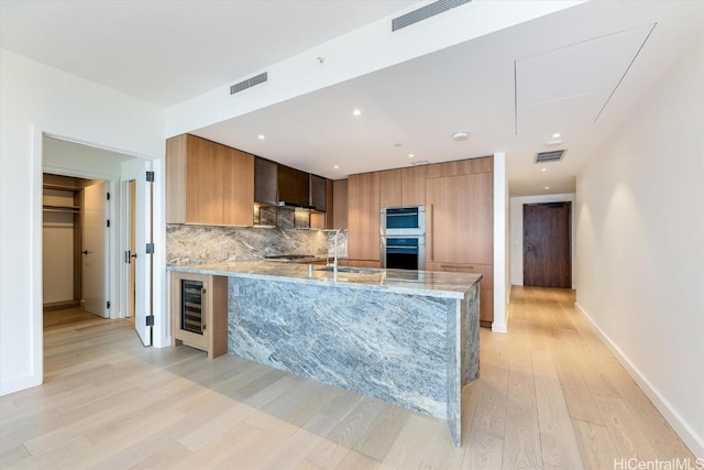 kitchen featuring appliances with stainless steel finishes, sink, wine cooler, light stone counters, and wall chimney range hood